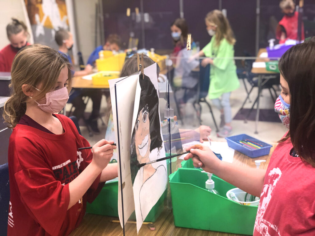 students using plexiglass dividers as easels to paint portraits